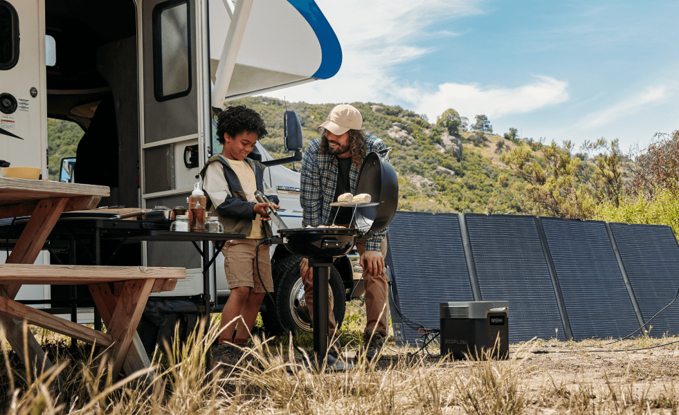 RV outdoors with man and child grilling food. DELTA 2 Max is charging via a solar panel.