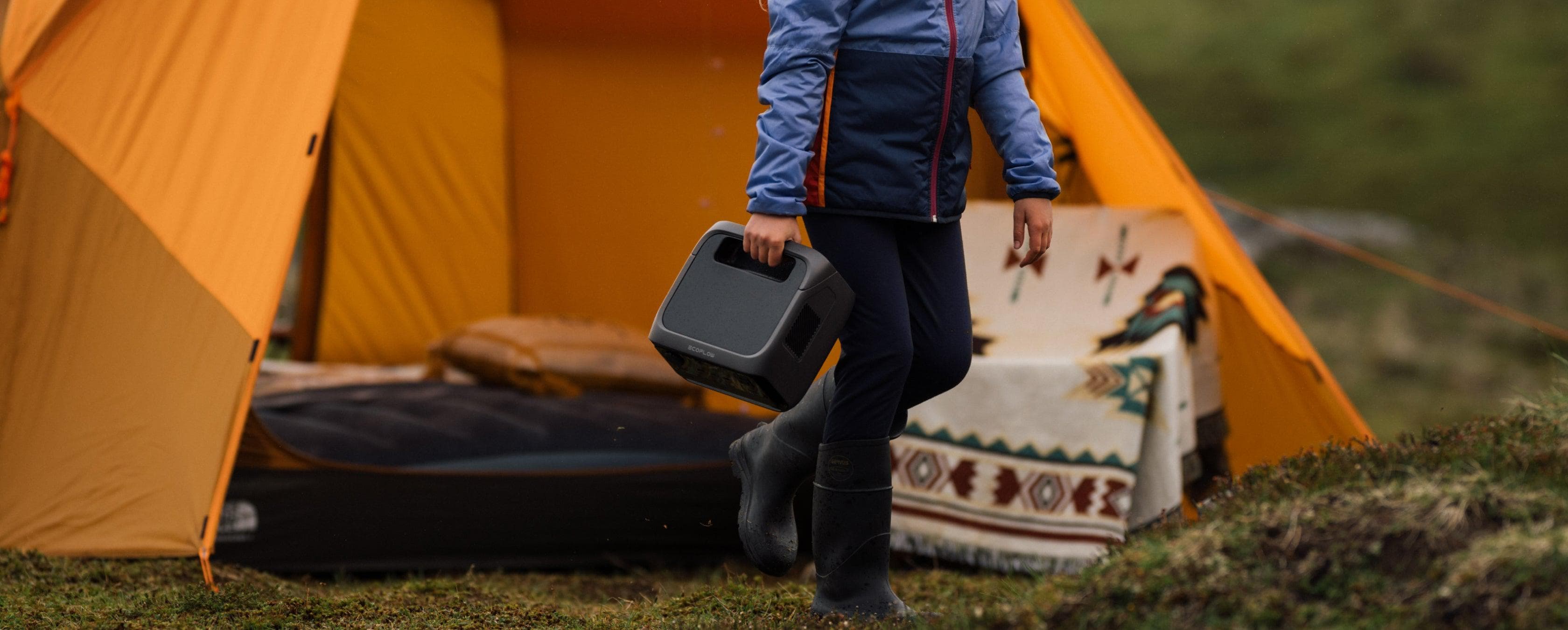 A camper carrying a compact EcoFlow portable power station beside a tent