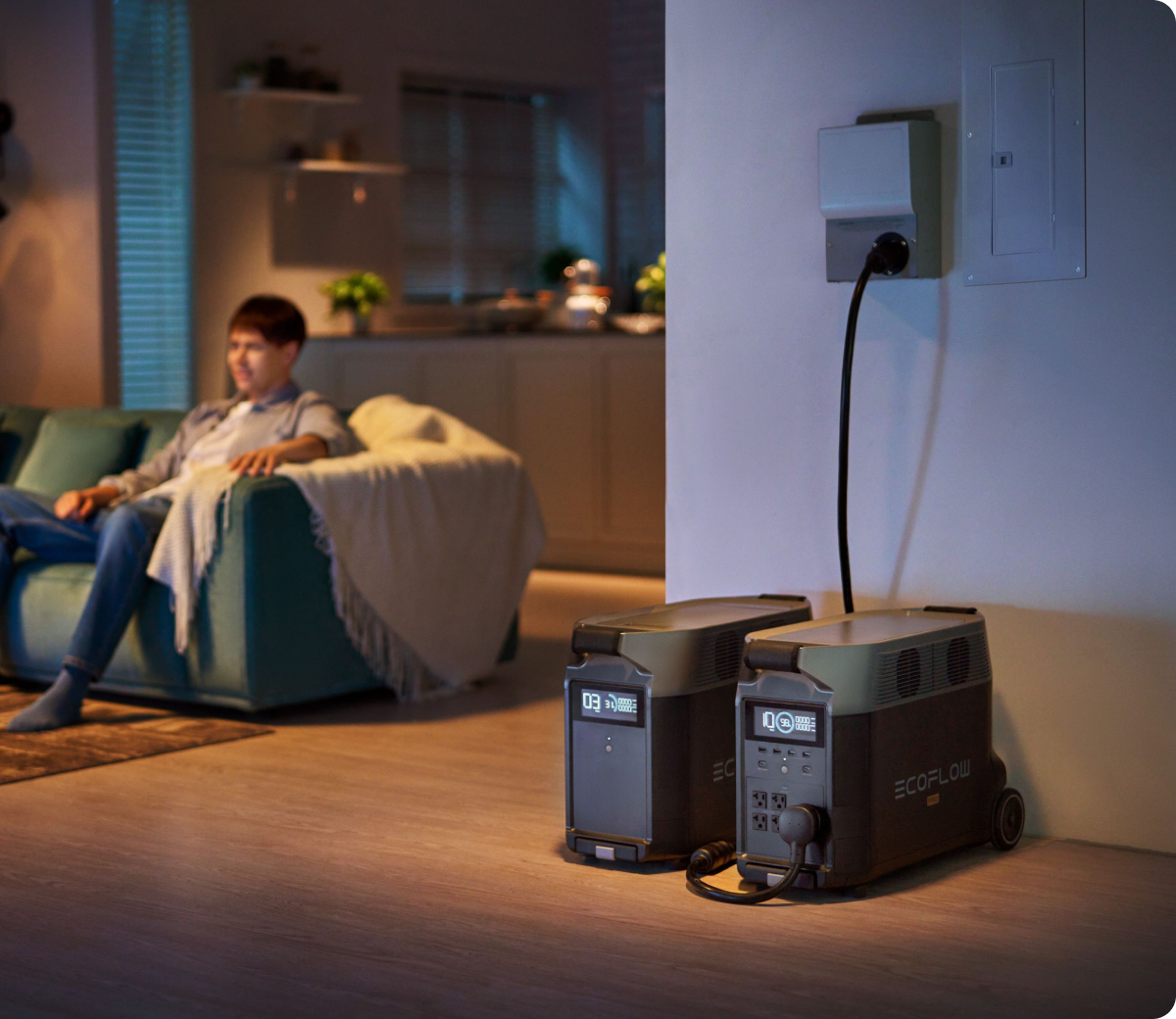 Two DELTA Pro batteries connected to a transfer switch inside a living area, while a man sits to the left.